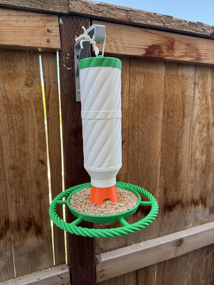 A white and green bird feeder hanging on a fence, created using 3D prints.