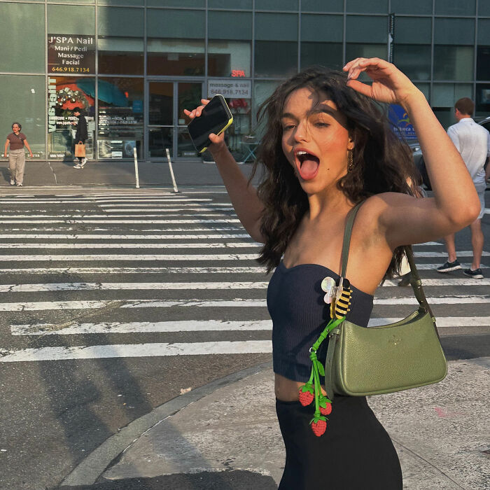 Rachel Zegler posing playfully with her mouth open while crossing a city street.