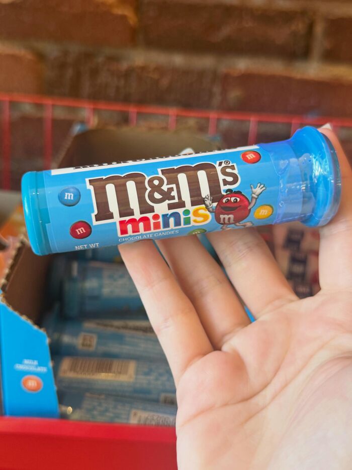 A hand holding a blue tube of M&M's Minis, a popular pick for the best Halloween candies list.