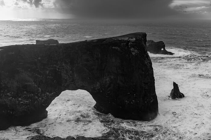 A massive natural rock arch along the coast of a black sand Iceland beach during a dramatic storm.
