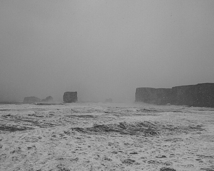 Misty ocean waters and distant sea stacks viewed from a stormy black sand Iceland shore.