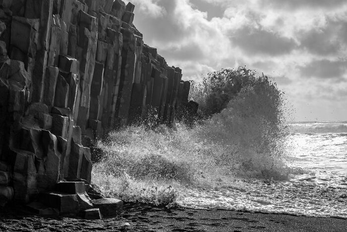 Crashing ocean waves against basalt column cliffs at a black sand Iceland beach in black and white.