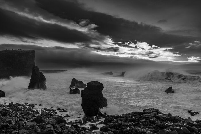 Dark, moody black and white coastline with giant rocks and stormy crashing waves at a black sand Iceland beach