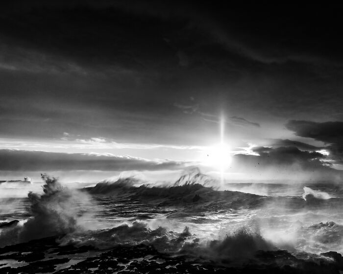 Black and white landscape of sun glaring over dramatic stormy ocean waves on a black sand Iceland shore