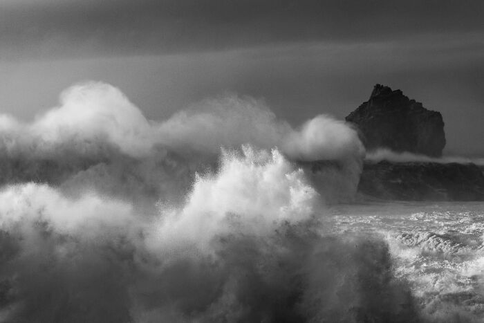 Dramatic black and white view of giant crashing waves and a sea stack near a black sand Iceland beach