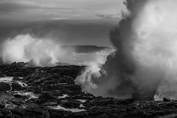Large ocean spray crashing against dark volcanic rocks on a black sand coast in Iceland
