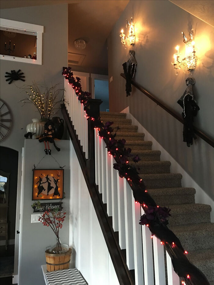 Spooky Halloween indoor staircase decor with black garland, lights, and hanging ghosts.