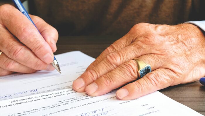 Close-up of a person signing legal documents for a life-changing inheritance with a blue pen. Close-up of a person signing legal documents for a life-changing inheritance with a blue pen.