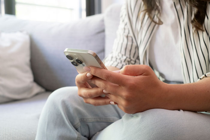 Woman holding a smartphone on couch, illustrating phone tracking concerns after cheating Woman holding a smartphone on couch, illustrating phone tracking concerns after cheating
