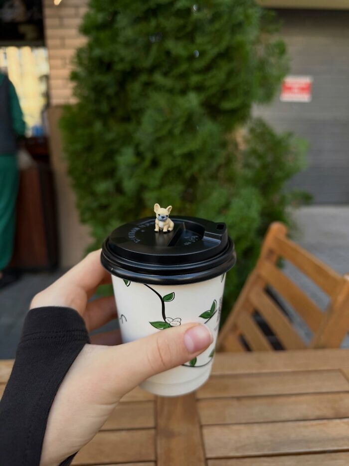 A close up of a hand holding a coffee cup with a tiny 3D printed puppy on the lid.