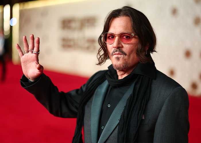 Johnny Depp waves to fans on a red carpet event, wearing glasses.