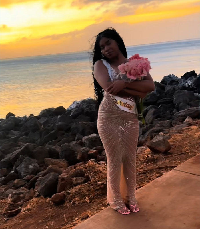 Woman in a sparkly dress holding flowers on a rocky beach defying local warnings