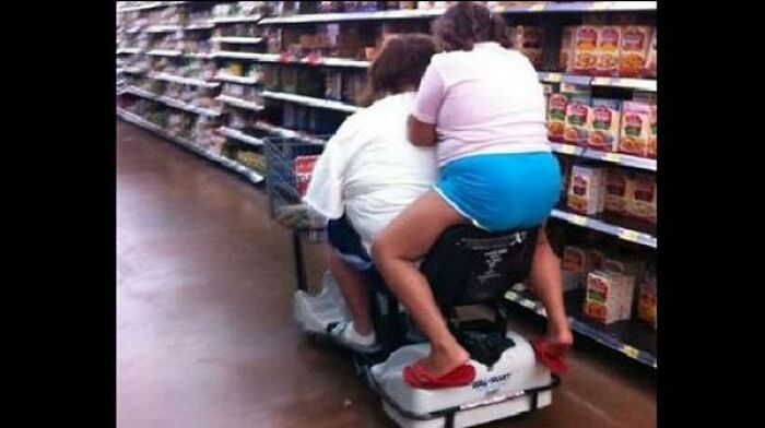 Two people riding single motorized Walmart scooter in aisle