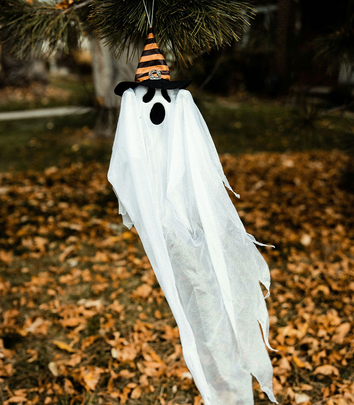 A white ghost hanging as a Halloween decoration from a tree branch.