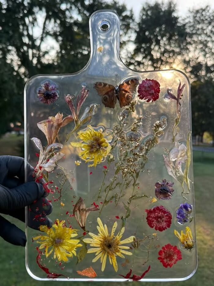 A clear resin cutting board with embedded dried flowers and a butterfly, an example of hilarious art projects.
