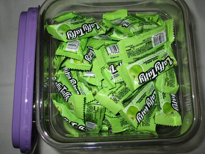 A clear plastic container filled with sour apple green Laffy Taffy candies for Halloween treats.