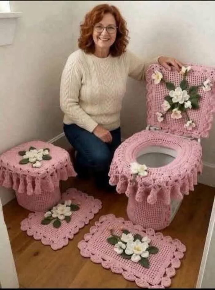 A woman proudly sitting next to her bizarre craft ideas featuring a fully crocheted pink toilet seat cover set.