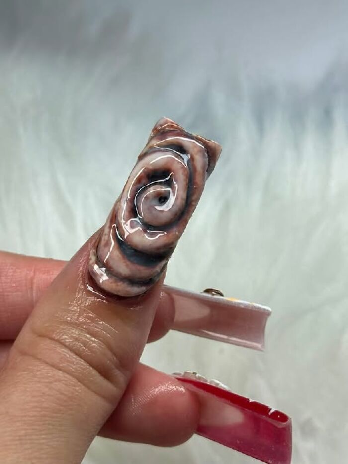 A strange art project featuring acrylic nail design made to look like a cinnamon roll.