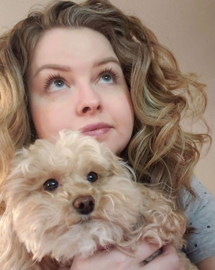 A woman with curly blonde hair and her fluffy dog looking up together, illustrating pets that look like their owners.