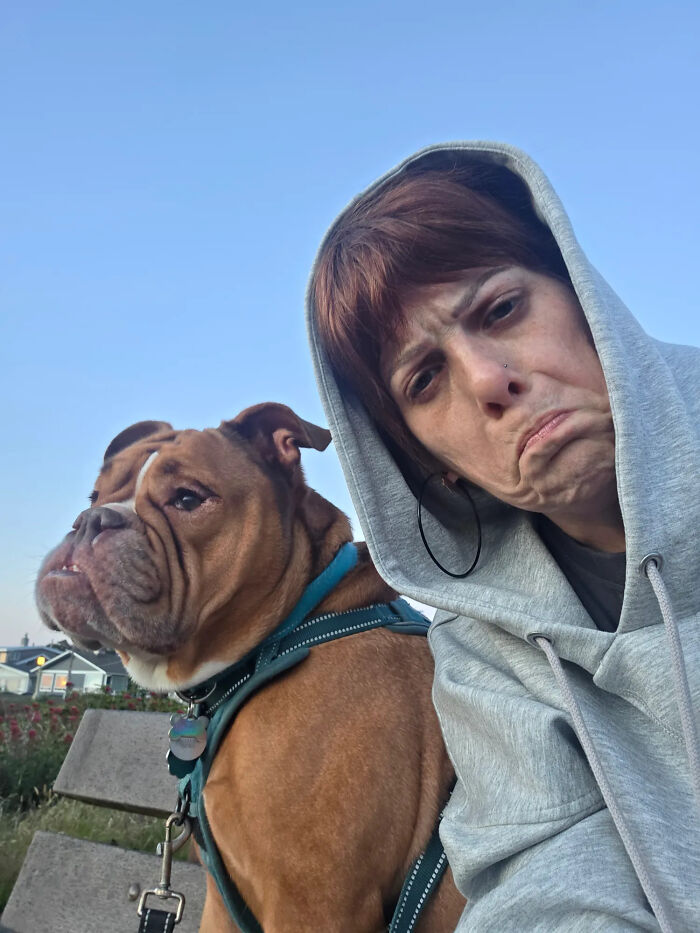 A woman in a grey hoodie and a bulldog making the same frowning face, showcasing pets that look like their owners.