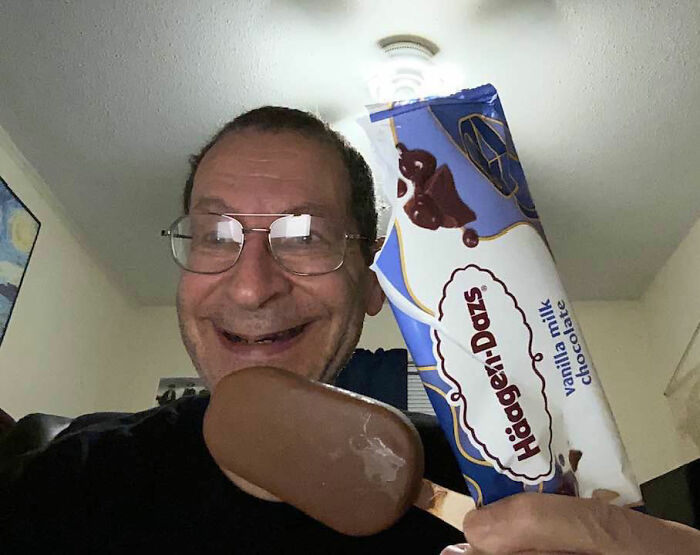 Former Grease star smiling and holding a chocolate-covered ice cream bar next to its packaging, sparking outrage.