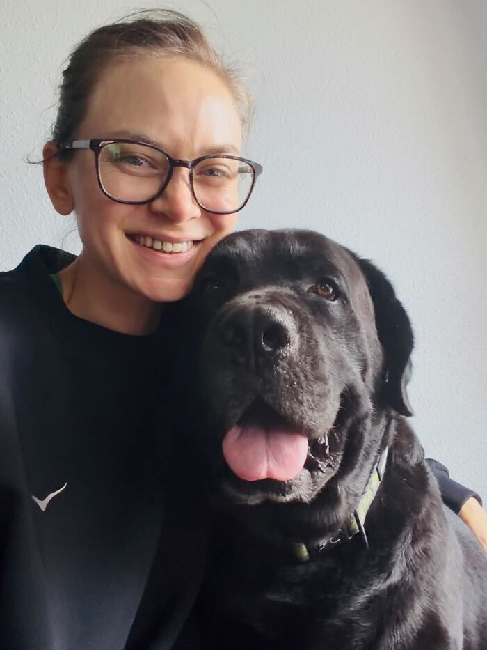 A smiling woman with glasses next to her happy black pet dog