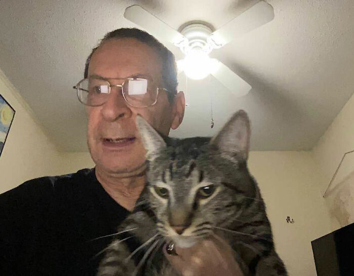 A close-up selfie of a middle-aged man wearing glasses while holding a domestic cat