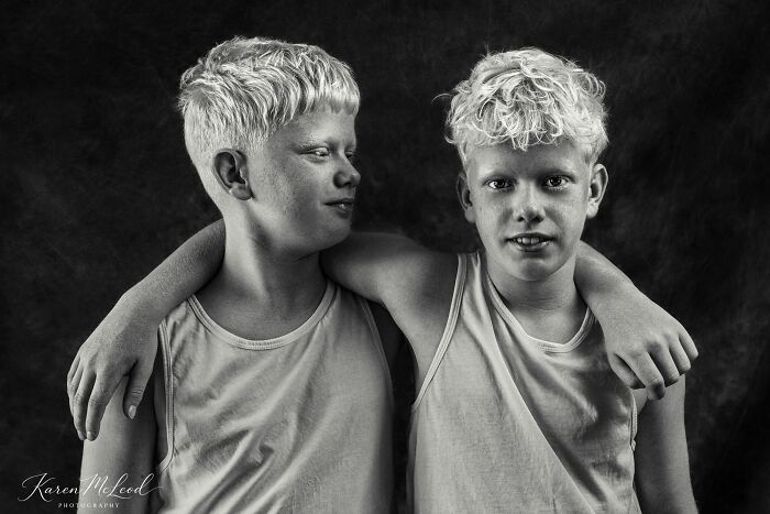A black and white portrait photo of two young boys with light curly hair hugging each other