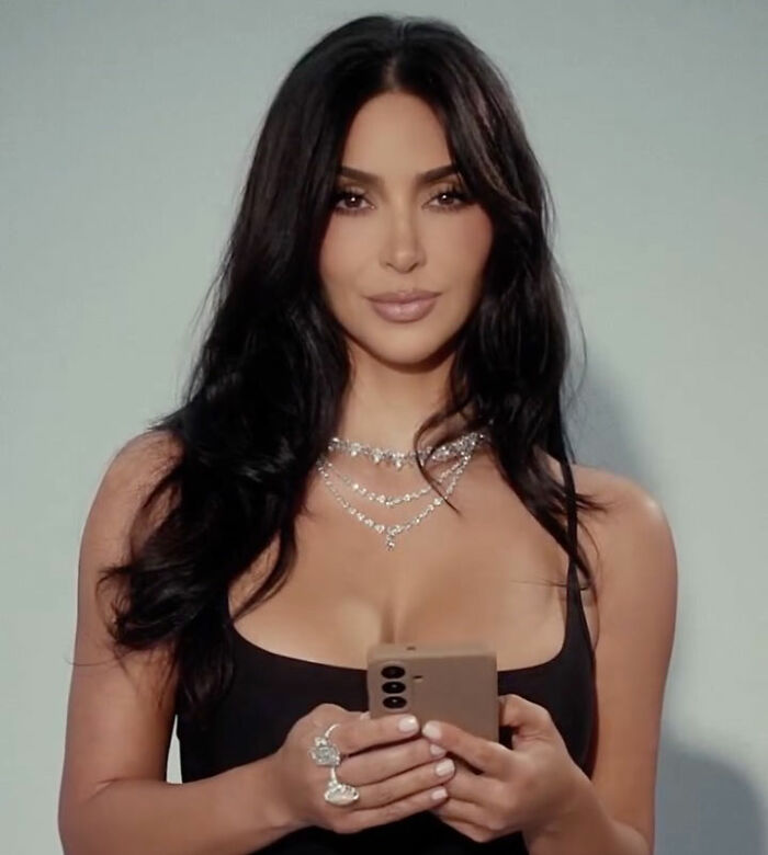 Kim Kardashian holding a phone wearing a black top and layered necklaces Kim Kardashian holding a phone wearing a black top and layered necklaces