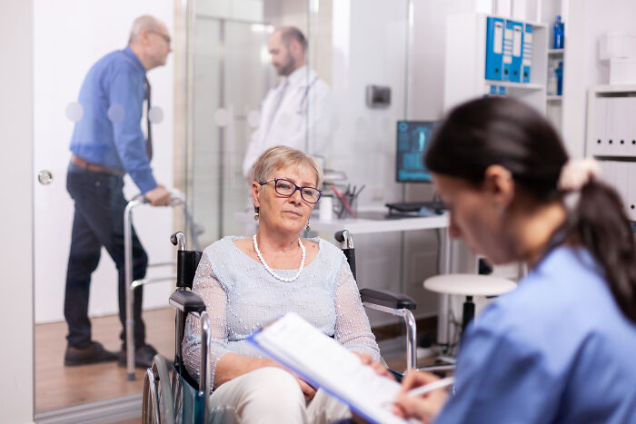 An elderly woman in a wheelchair speaking with healthcare workers in a clinic.