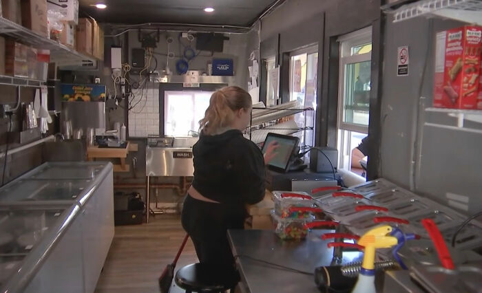 A teen employee working inside the ice cream shop, managing orders on a screen. A teen employee working inside the ice cream shop, managing orders on a screen.