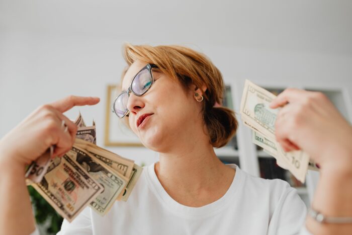A woman holding fans of cash celebrating her new life after receiving a life-changing inheritance. A woman holding fans of cash celebrating her new life after receiving a life-changing inheritance.