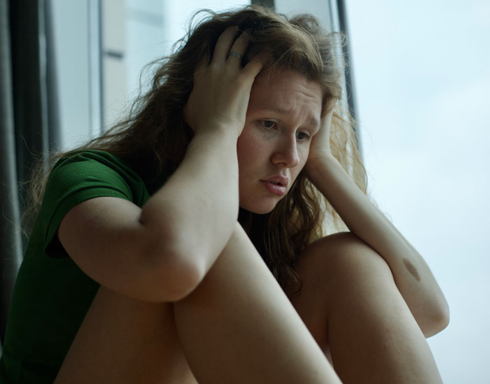 Worried woman sitting by window, reflecting distress about phone tracking Worried woman sitting by window, reflecting distress about phone tracking