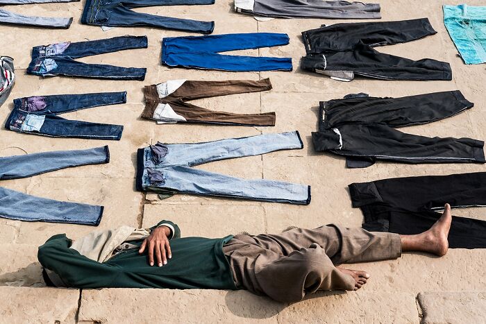 Man lying among neatly arranged jeans on ground in creative photography