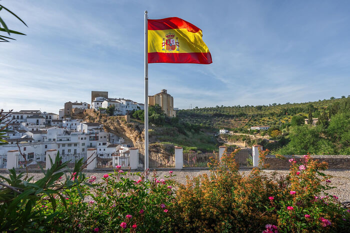 Spanish flag flying over a scenic village, illustrating partner's geography blunders questioning intelligence