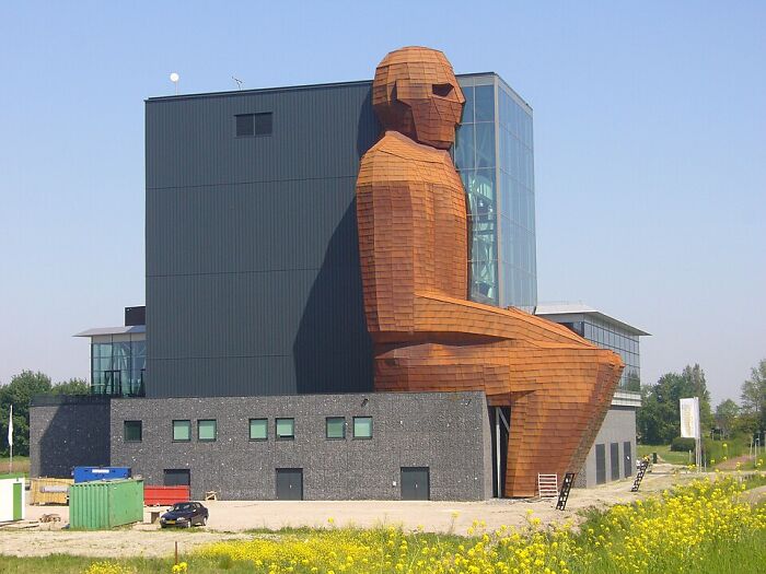 Giant seated wooden man sculpture integrated with modern building strange buildings