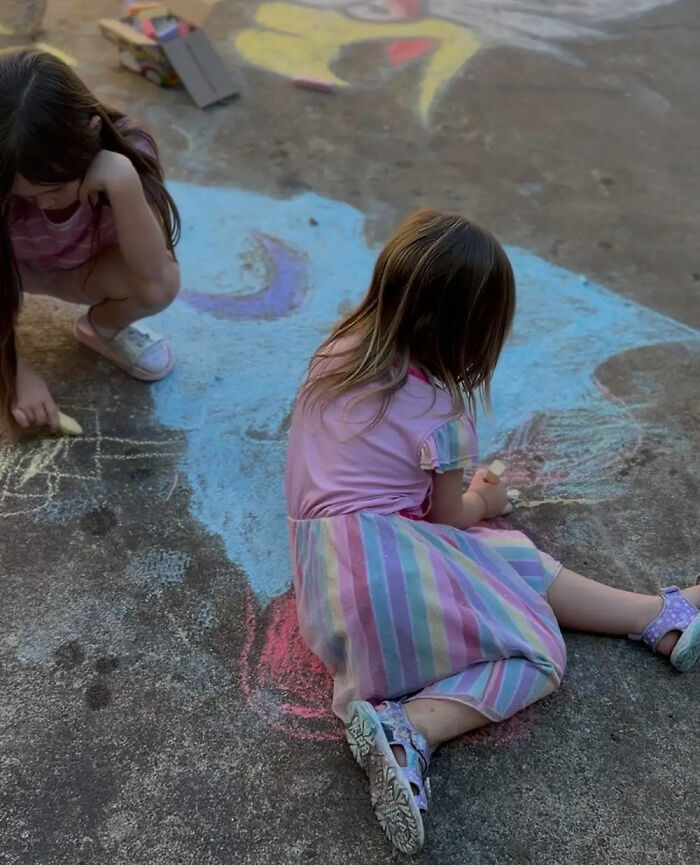 Two young girls playing and drawing with colorful sidewalk chalk outside, related to a school story about a 6YO daughter.