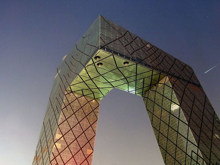 Modern skyscraper with a large geometric archway and crisscross window patterns at night