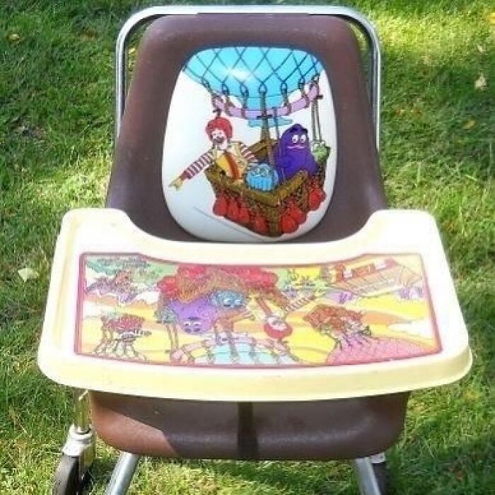 A nostalgic vintage McDonalds high chair featuring Ronald McDonald and Grimace on the backrest