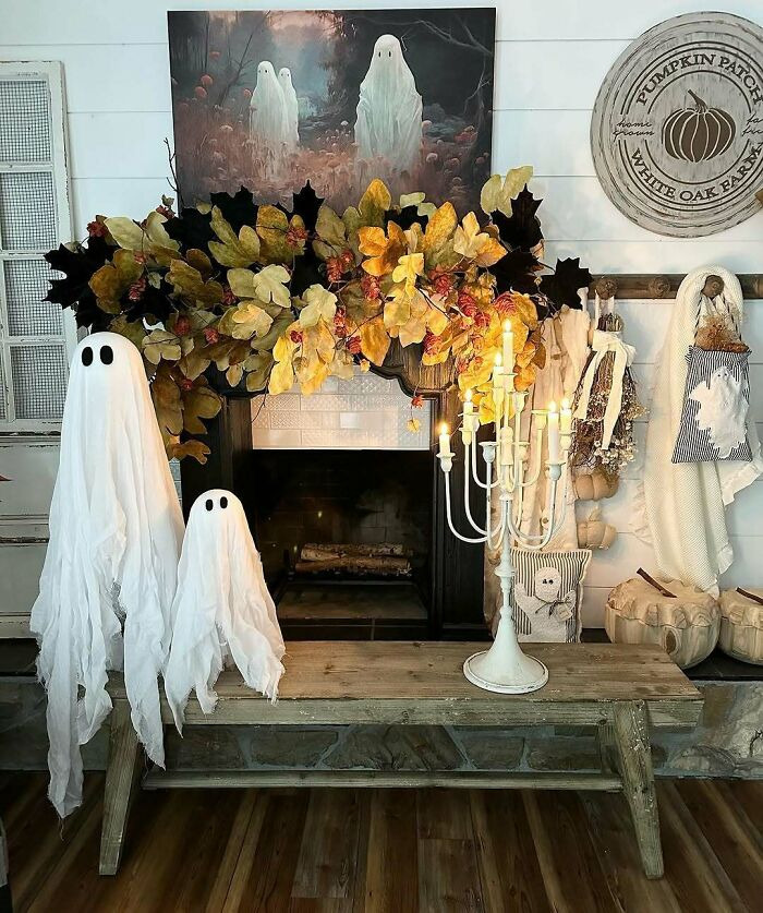 Rustic Halloween home setup featuring white ghost statues, autumn leaves, and a candelabra.