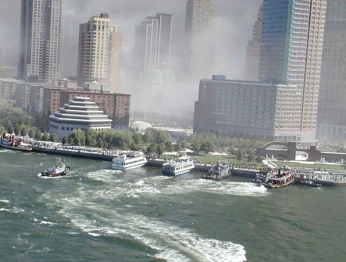 Rescue boats on river near urban skyscrapers with crowds watching in a city waterfront scene