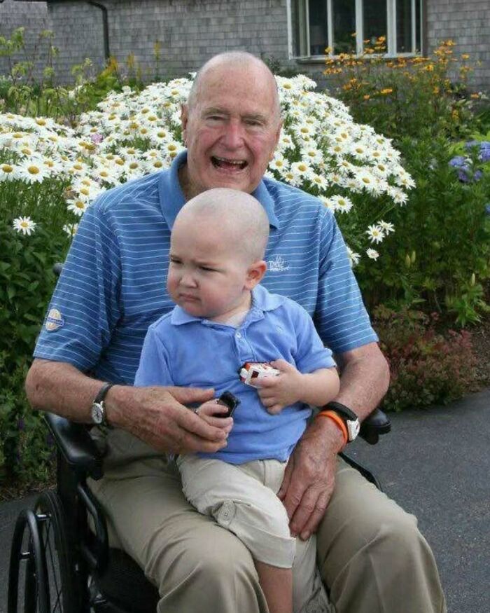 Elderly man in wheelchair smiling with young child outdoors