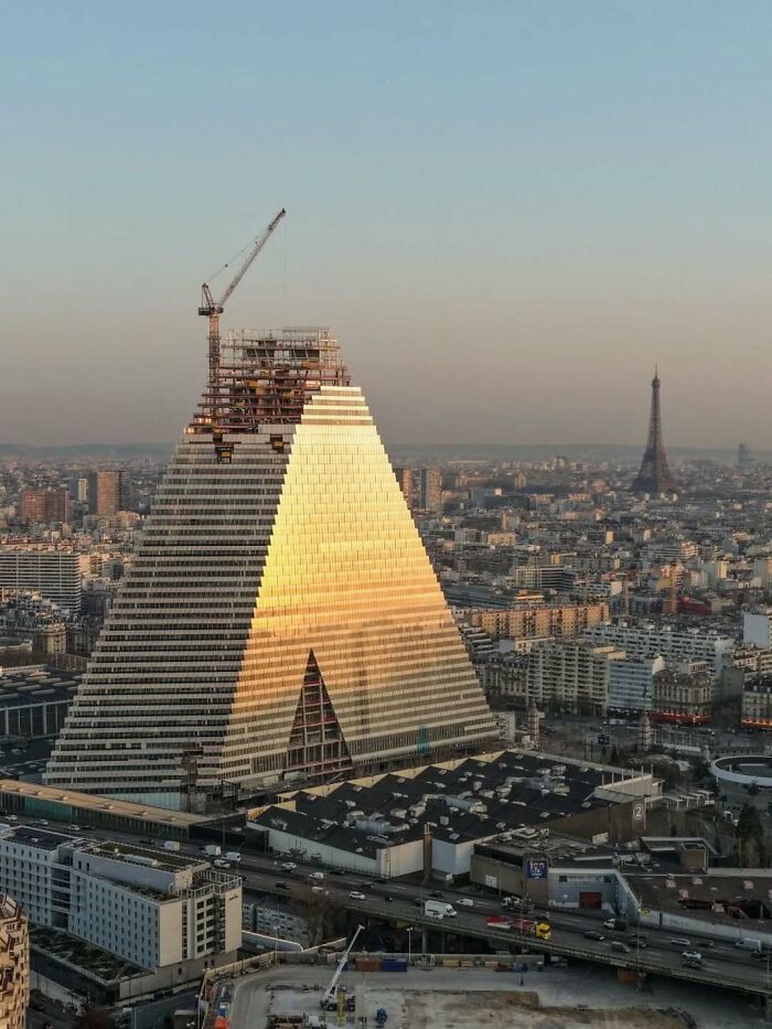 Pyramid-shaped strange building under construction with city and Eiffel Tower background