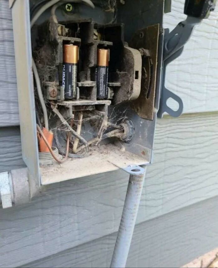 An outdoor electrical box with AA batteries inserted as fuses during questionable DIY projects.