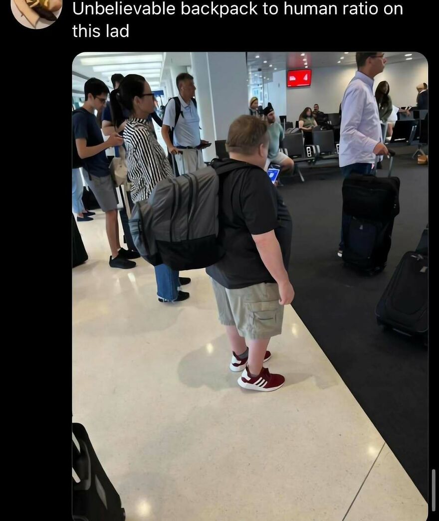 An out-of-context pic of a person standing at an airport wearing a huge backpack that is almost as big as them.