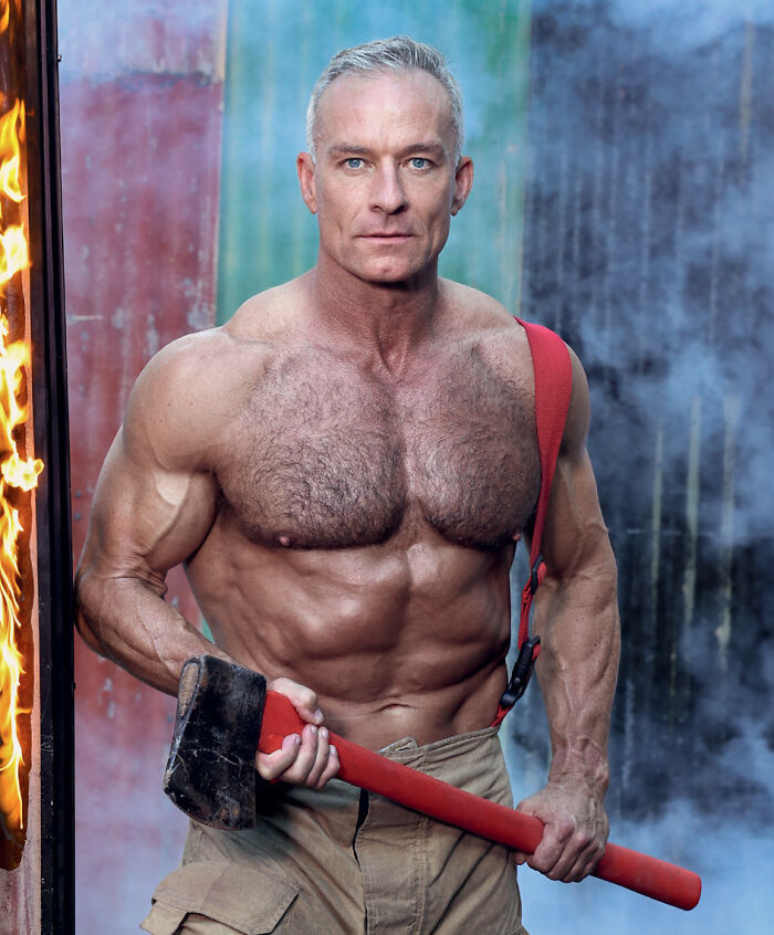 Muscular Australian firefighter holding an axe near flames for 2027 firefighter calendar