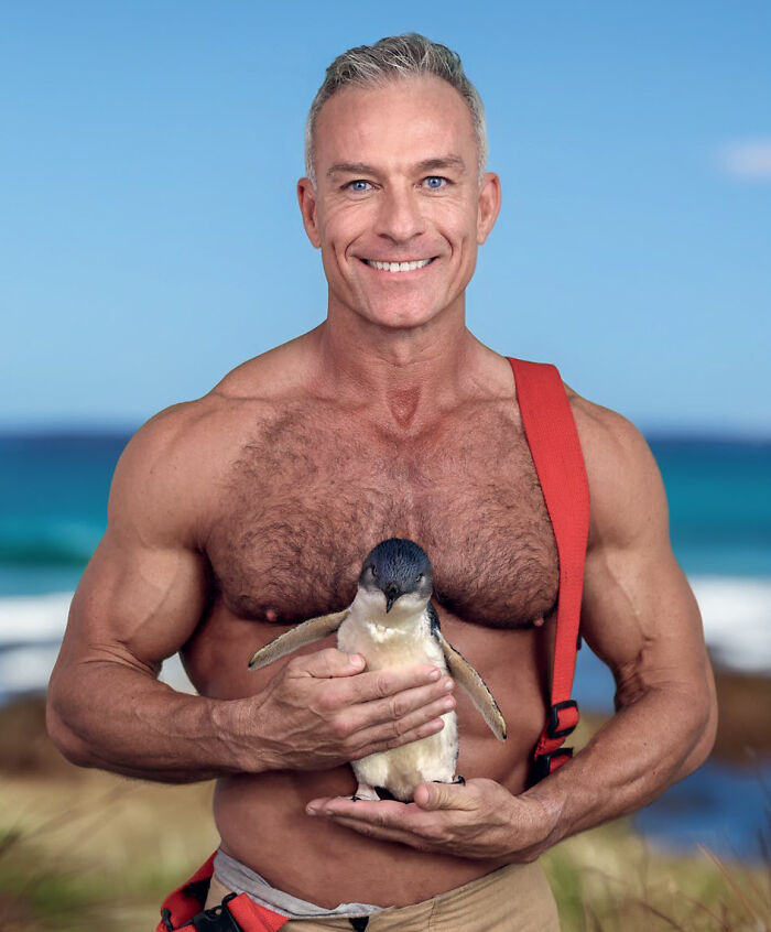 Smiling Australian firefighter holding a little penguin by the ocean