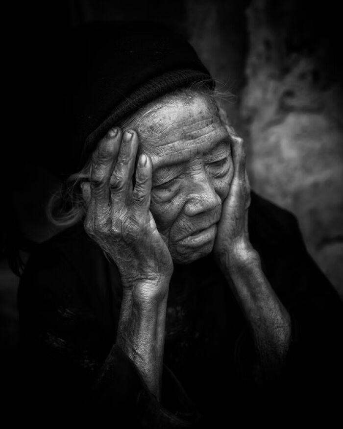 Black and white portrait photo of an elderly person holding their face, capturing a deep, emotional human expression.