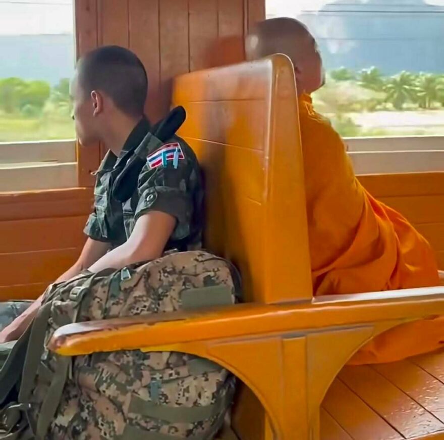 Out-of-context pics of a soldier and a Buddhist monk sitting back to back on a wooden train seat