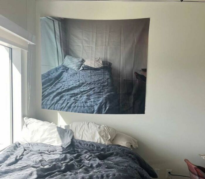 A wall tapestry printed with a photo of a bed hanging directly above a real bed in an amusing post
